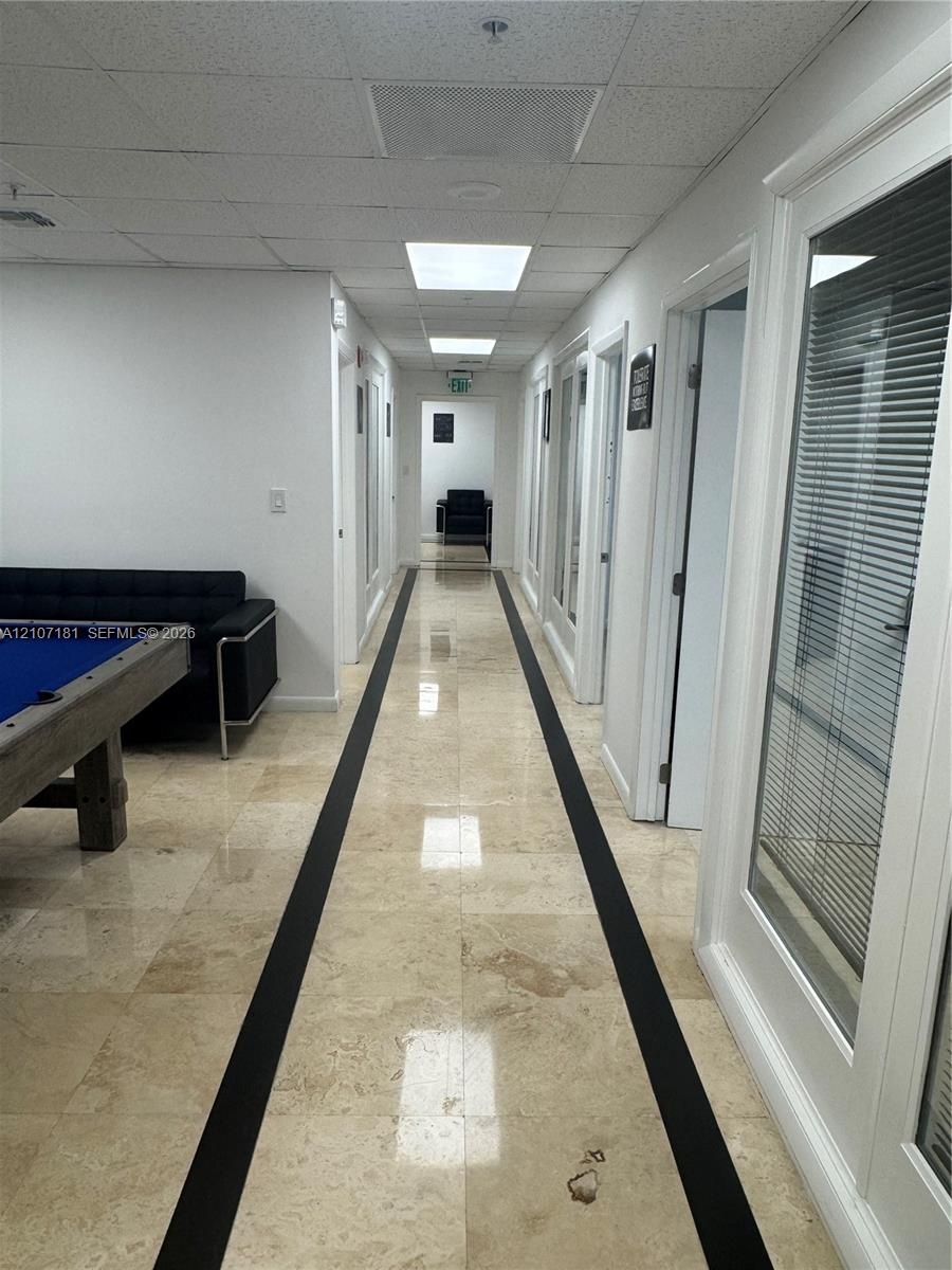 Hallway featuring polished stone tile flooring with decorative dark inlay, recessed lighting, and multiple doors with glass-panel inserts