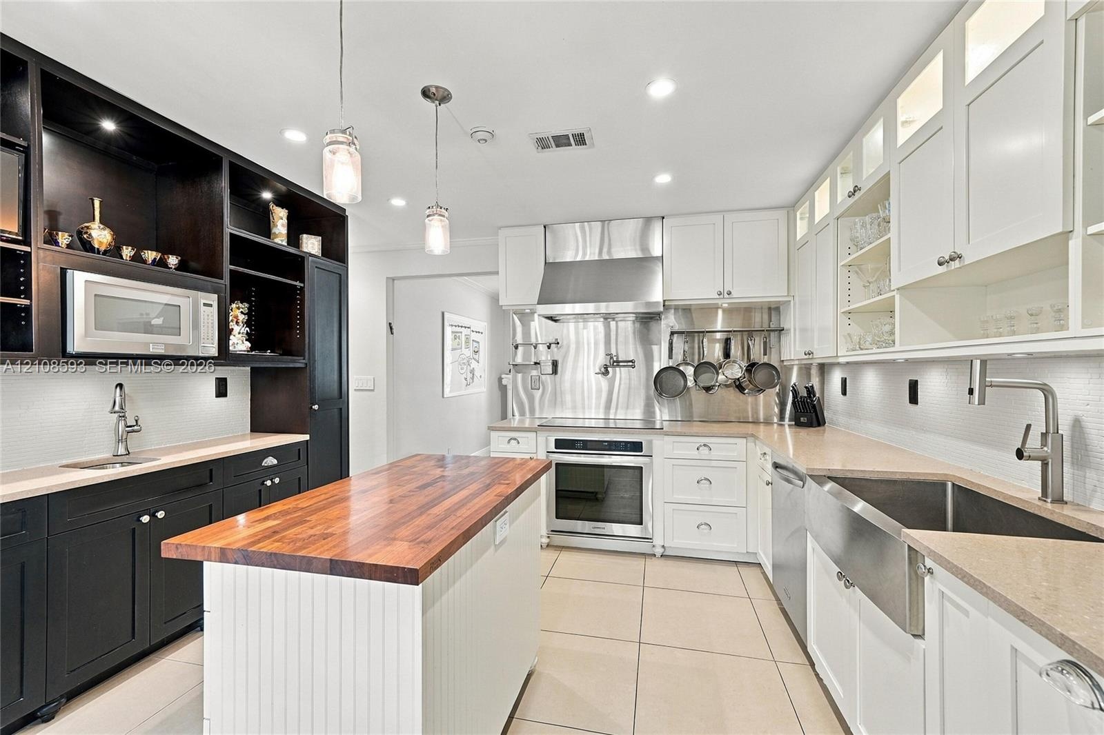 Kitchen featuring high-contrast cabinetry, butcher block island countertop, professional-grade stainless steel range hood, apron-front sink, and tiled