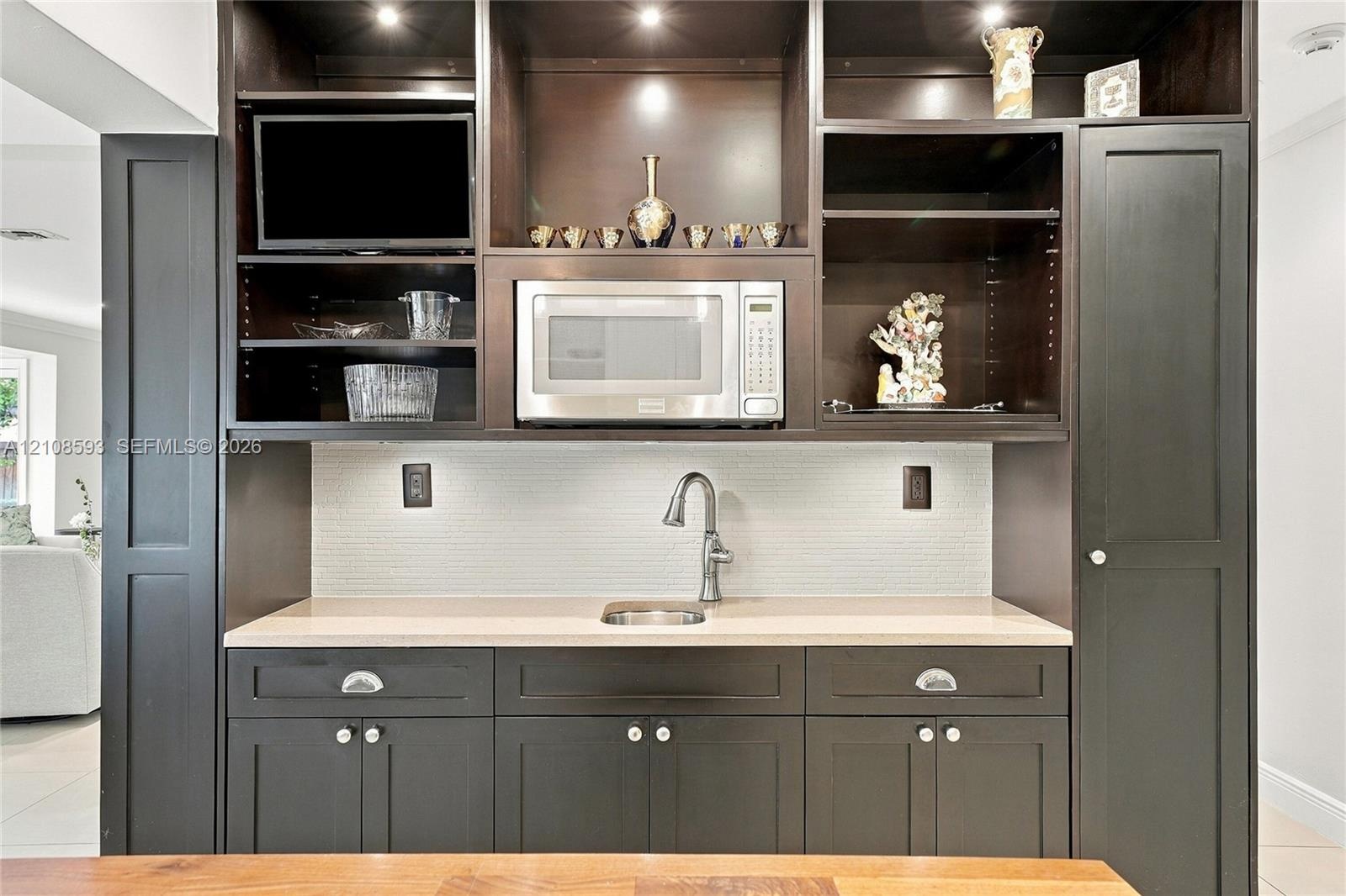Built-in cabinetry featuring dark finish, recessed task lighting, integrated microwave, stone-finish countertop, and undermount stainless steel sink w