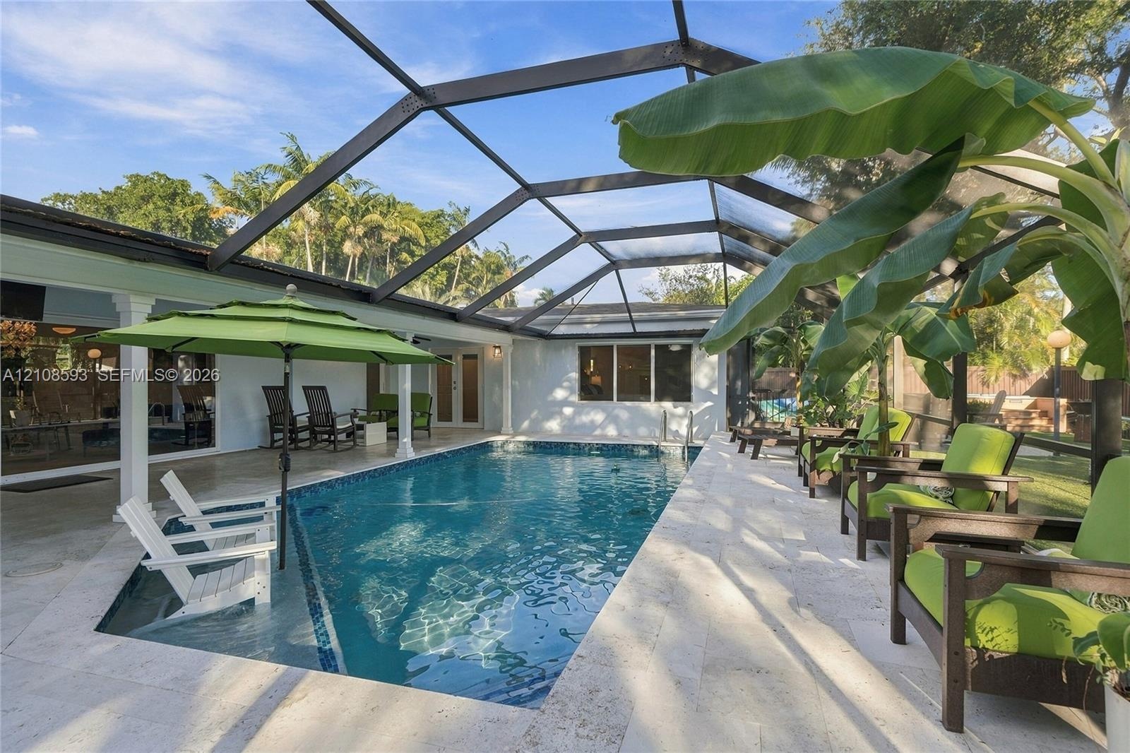 Screen-enclosed swimming pool featuring a Baja shelf, natural stone patio, and covered patio area