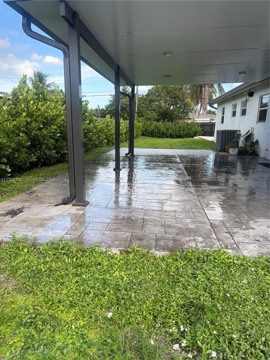 Covered patio featuring stamped concrete flooring, a solid roof structure, and perimeter shrubbery