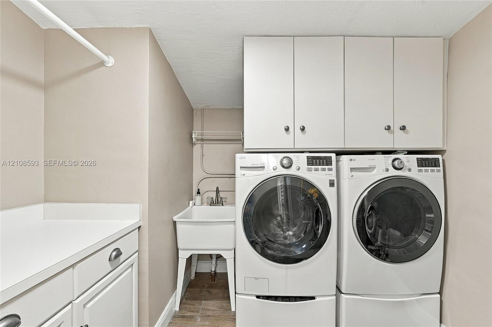 Laundry room featuring white cabinetry, a utility sink, countertop workspace, and overhead storage