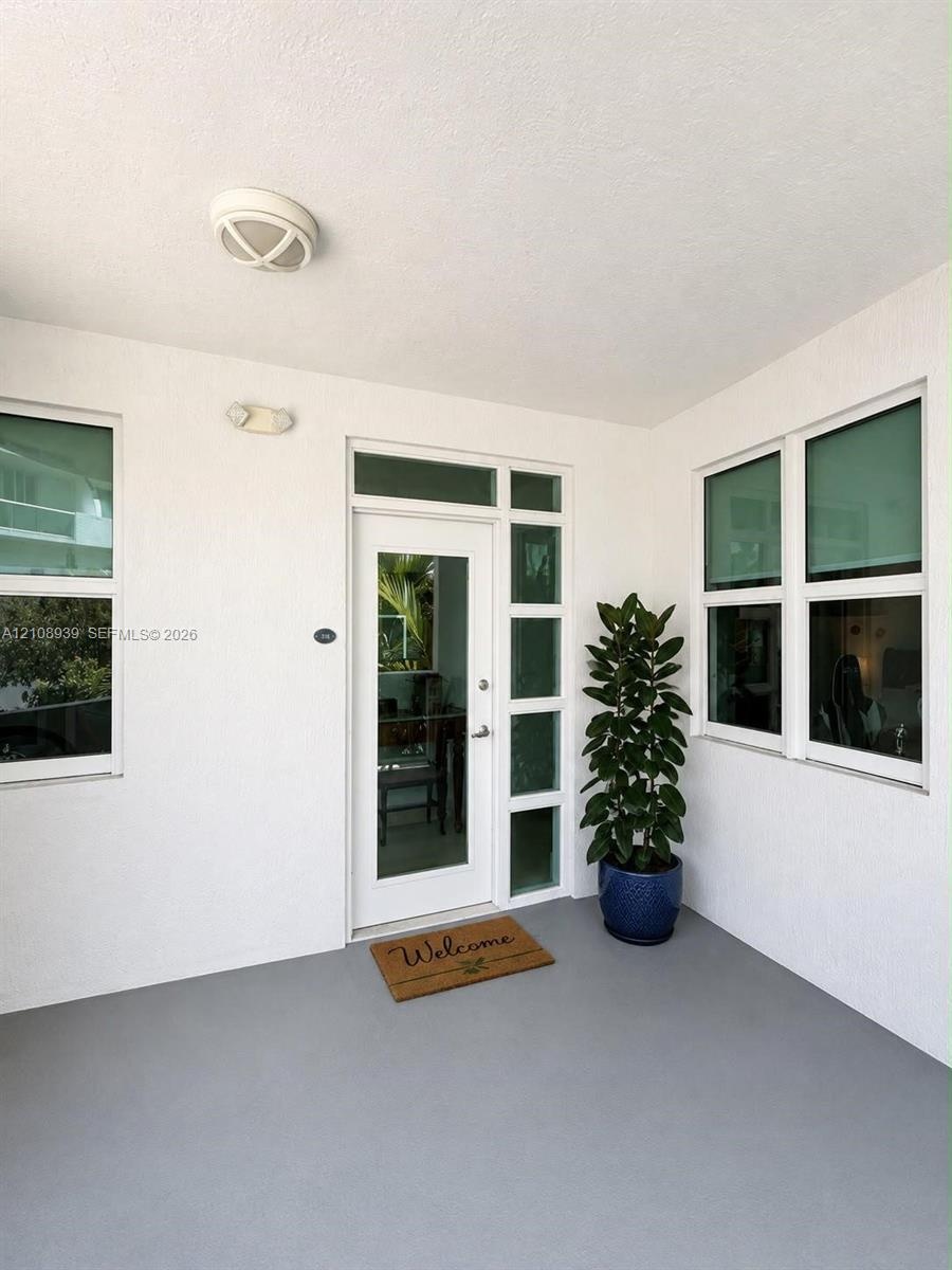 Covered porch entry featuring a glass-panel front door with vertical sidelights, textured exterior walls, smooth-finish flooring, and multiple dual-pa