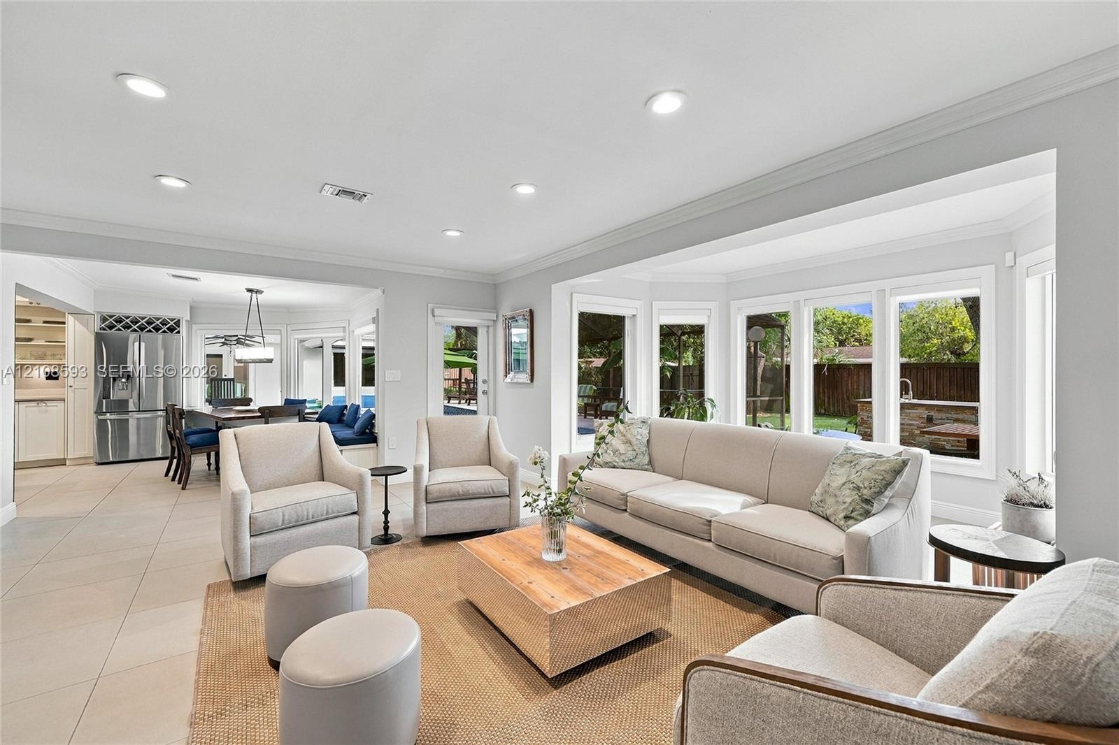 Open-concept space featuring oversized bay windows, neutral tile flooring, recessed lighting, and crown molding