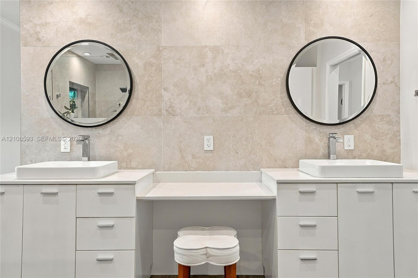 Dual white cabinetry with white stone countertops, integrated center vanity station, dual vessel sinks, wall-mounted round mirrors with matte black fr
