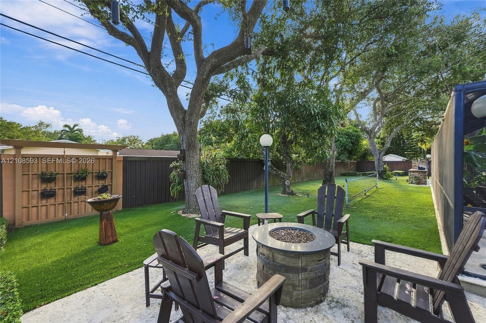Backyard featuring a stone-paver patio, built-in circular stone fire pit, wood-lattice privacy screen, and mature trees
