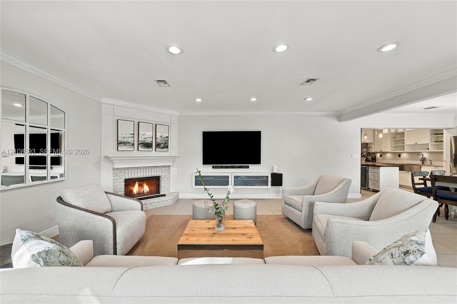 Living area featuring a painted brick corner fireplace with a mantel, recessed ceiling lighting, crown molding, and built-in cabinetry