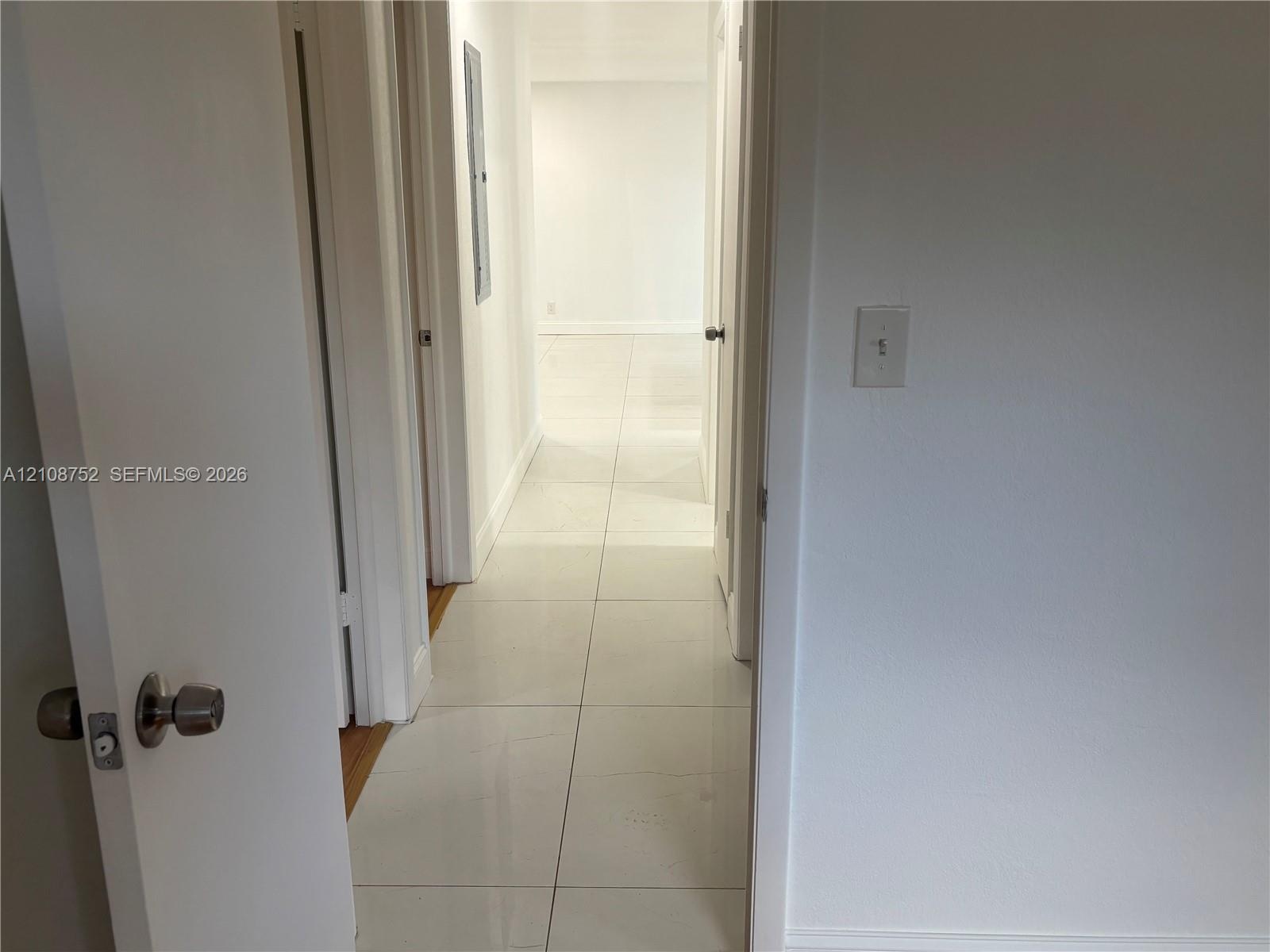Interior hallway featuring large-format ceramic tile flooring, neutral wall finishes, and solid-core interior doors with satin nickel hardware