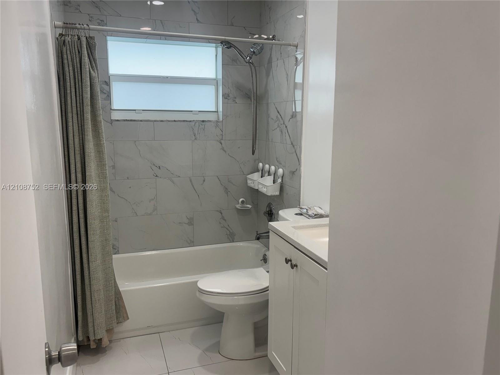 Bathroom featuring full-height stone-finish wall tile, a built-in bathtub, a shaker-style vanity with an integrated basin, and a window