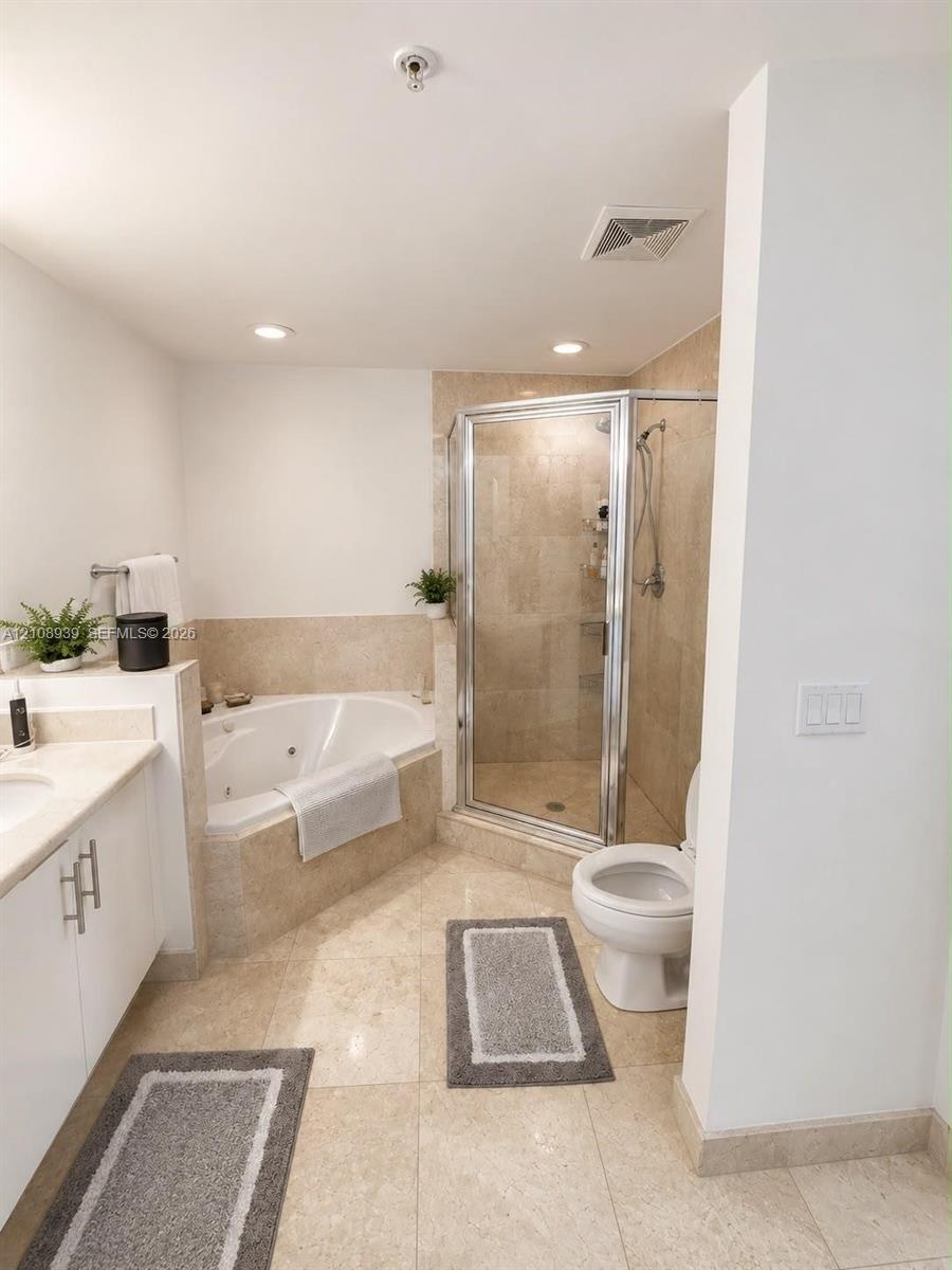 Bathroom featuring a jetted corner soaking tub, a tiled walk-in shower with a glass enclosure, stone-surround finishes, a white vanity with hardware, 