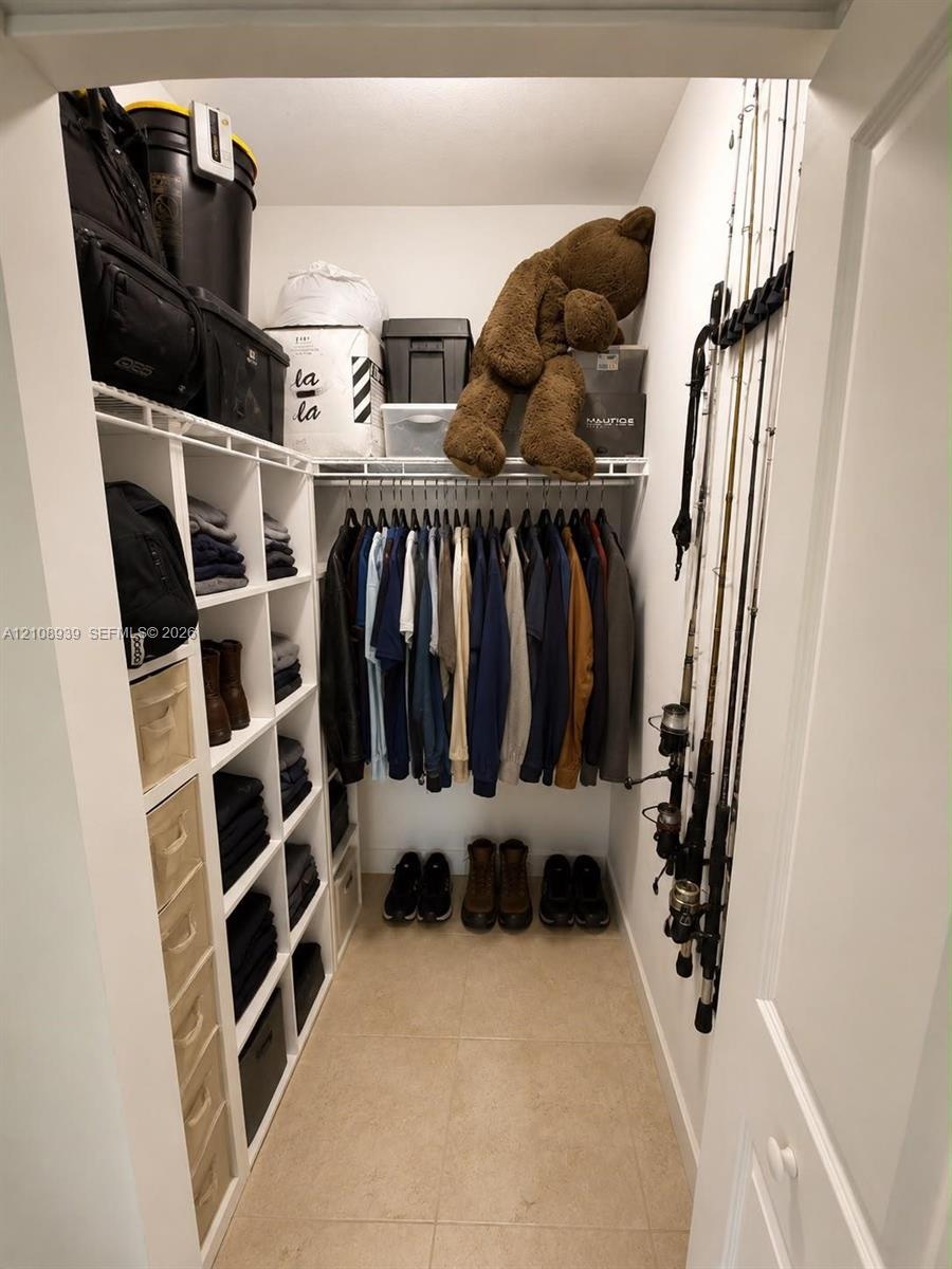 Walk-in closet featuring white built-in vertical shelving, integrated wire hanging rods, and tile flooring