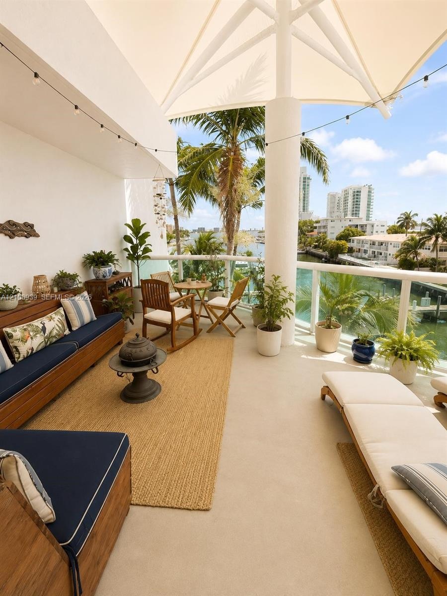 Covered terrace featuring a tensile fabric shade structure, glass panel railing, and concrete flooring, overlooking a water-facing landscape with matu