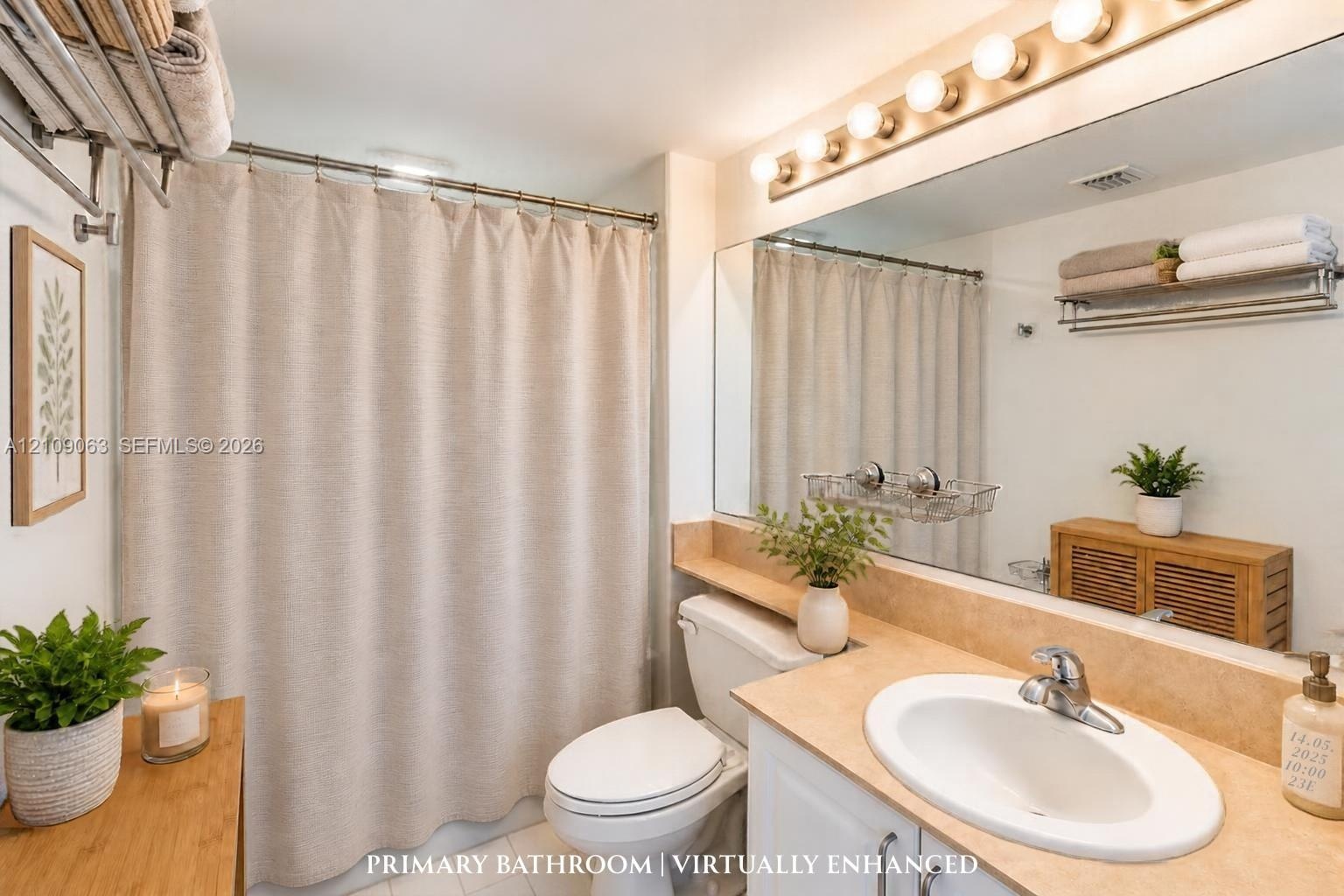 Bathroom featuring a vanity with a neutral-tone countertop, oval undermount sink, expansive wall-to-wall mirror, multi-bulb vanity lighting, and a sho