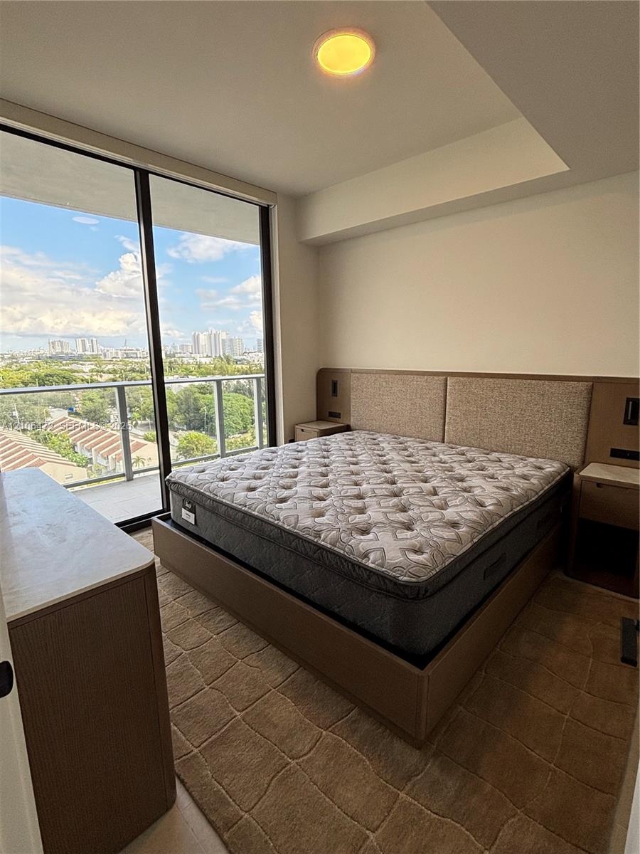 Floor-to-ceiling glass sliding doors, private balcony with metal railing, built-in wooden headboard with integrated lighting and electrical outlets, r