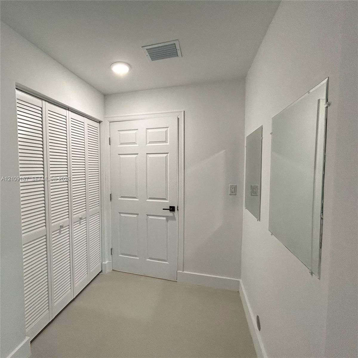 Six-panel interior door with matte black hardware, floor-to-ceiling louvered closet doors, and wall-mounted mirrors