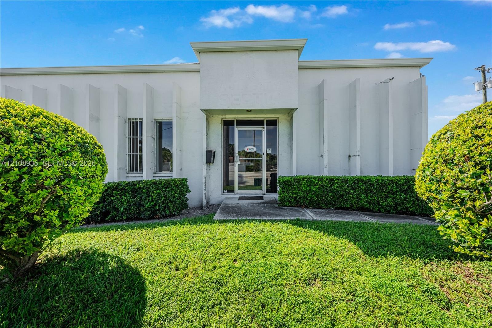 Stucco exterior featuring vertical structural fins, aluminum-framed glass entry door, and manicured landscaping