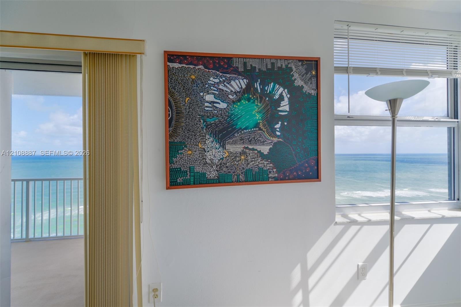 Floor-to-ceiling sliding glass doors, multi-pane window with horizontal blinds, and private balcony with metal railing, showcasing an expansive ocean 