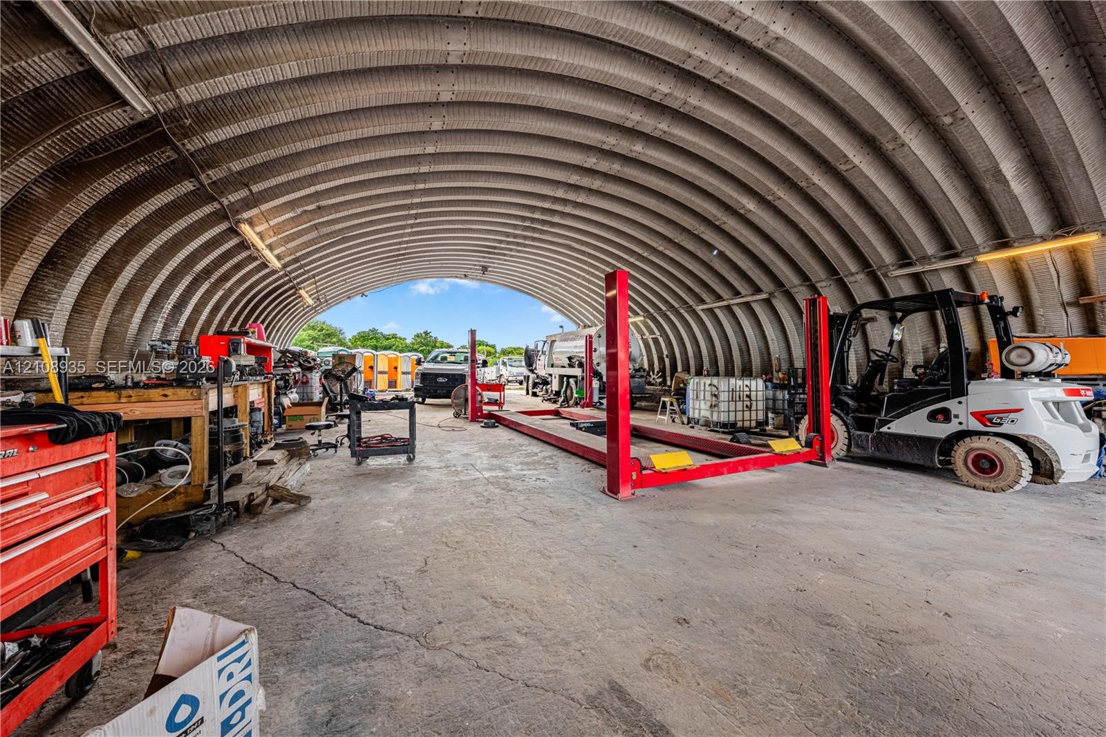 Quonset-style structure featuring a high-clearance arched metal roof, concrete flooring, and a built-in automotive lift system