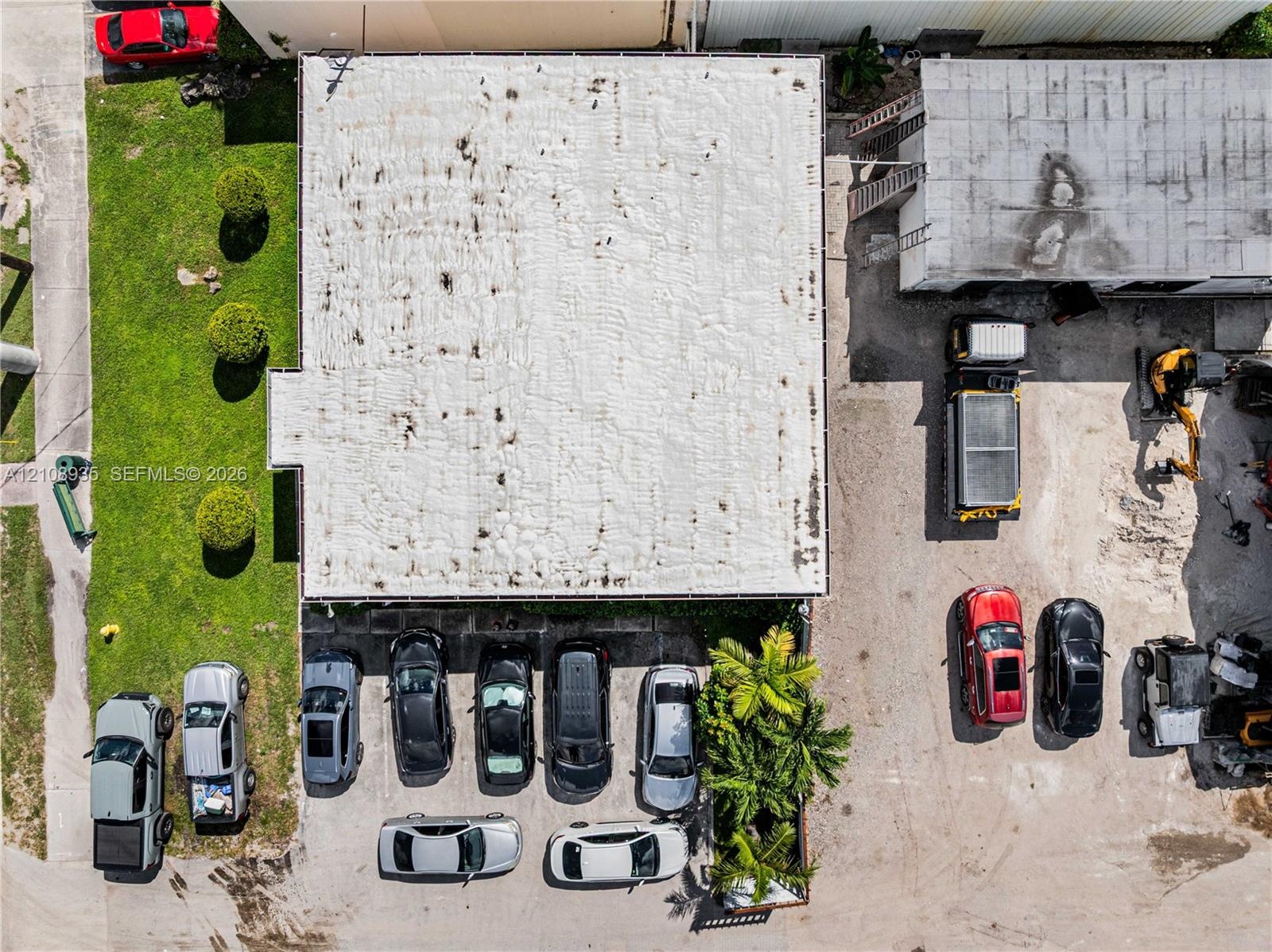 Aerial perspective featuring a commercial structure with an expansive paved surface area, dedicated on-site parking spaces, and manicured green space