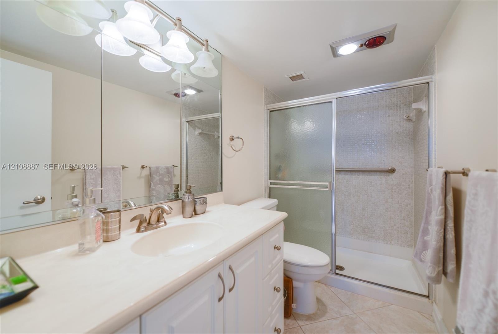 White vanity cabinetry featuring a light-toned countertop with integrated sink, full-width mirror, five-bulb integrated vanity lighting, and walk-in s