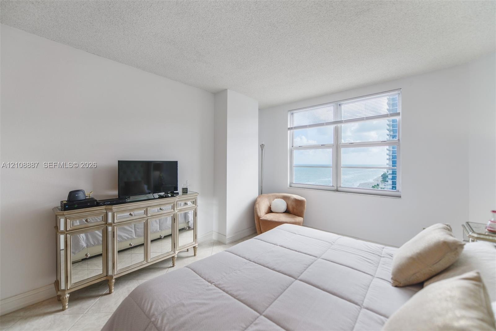 Neutral-toned interior featuring expansive horizontal windows with ocean and coastal horizon scenery, light-colored tile flooring, and textured ceilin