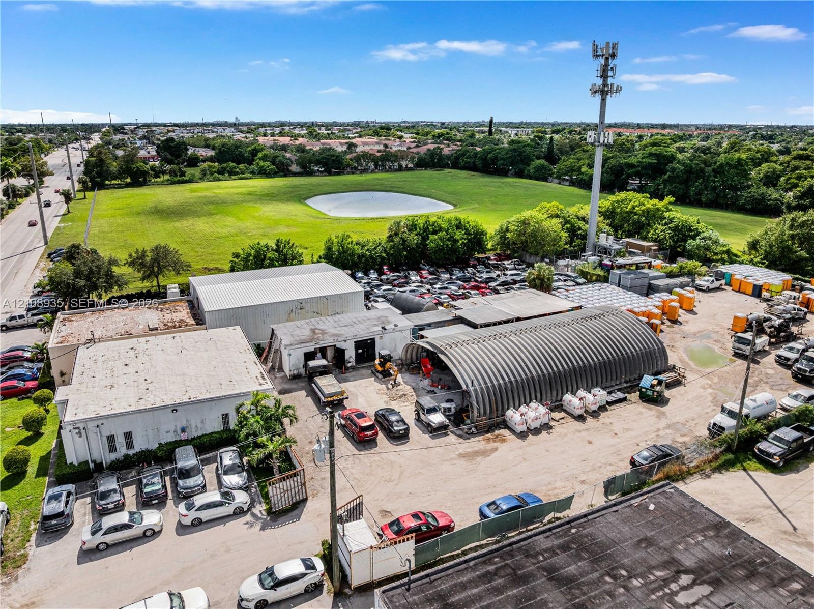 Industrial property featuring multi-structure layout with arched metal storage building, paved surface parking, and extensive open land