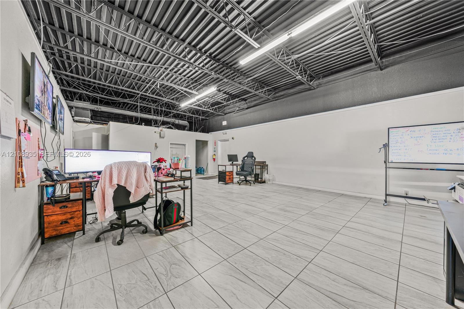 Open-concept interior featuring light-toned ceramic tile flooring, an industrial-style exposed ceiling, and linear fluorescent lighting