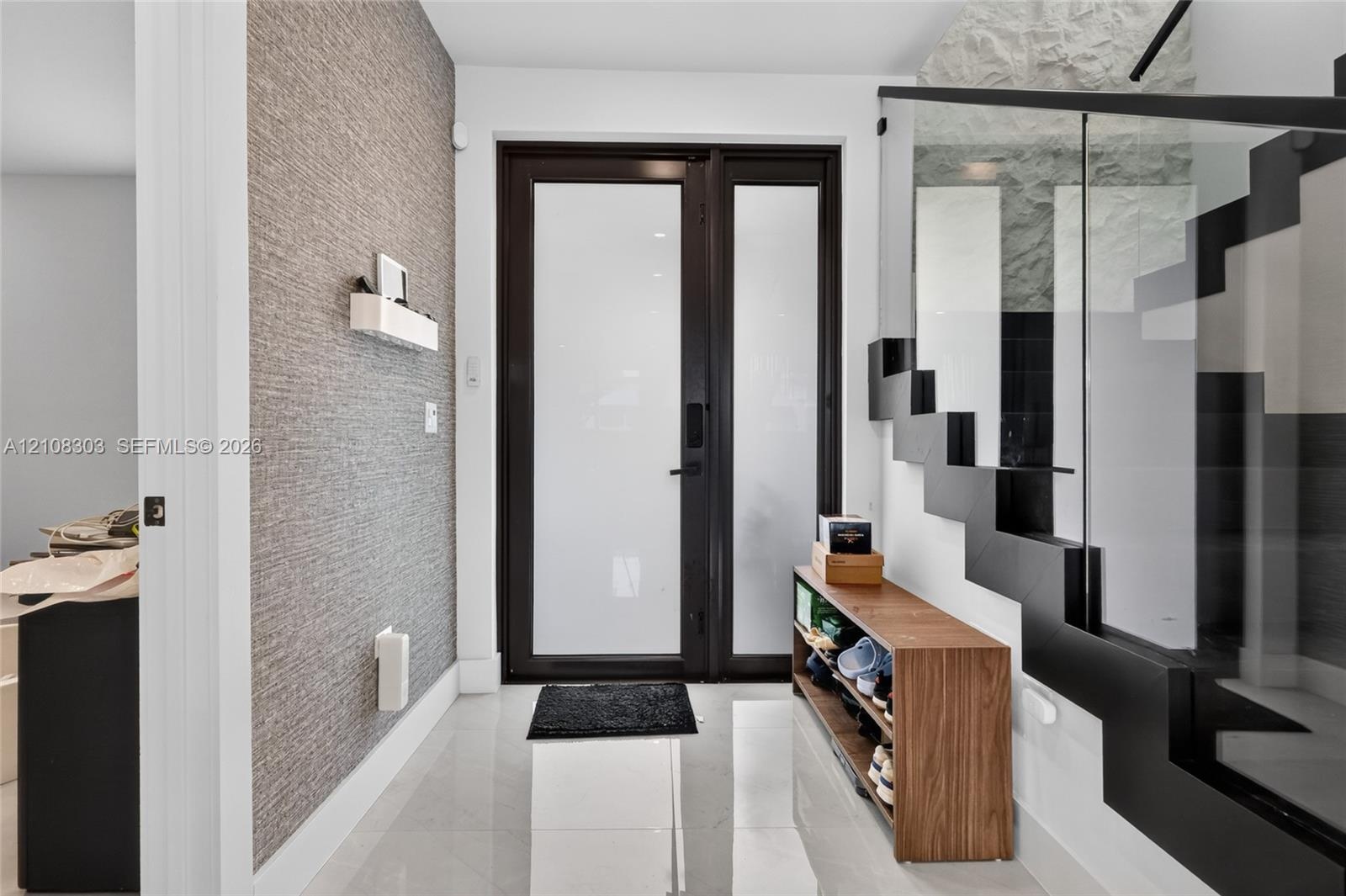 Entryway featuring a black-framed glass entry door, large-format tile flooring, textured wall covering, and a staircase with open risers and a glass r