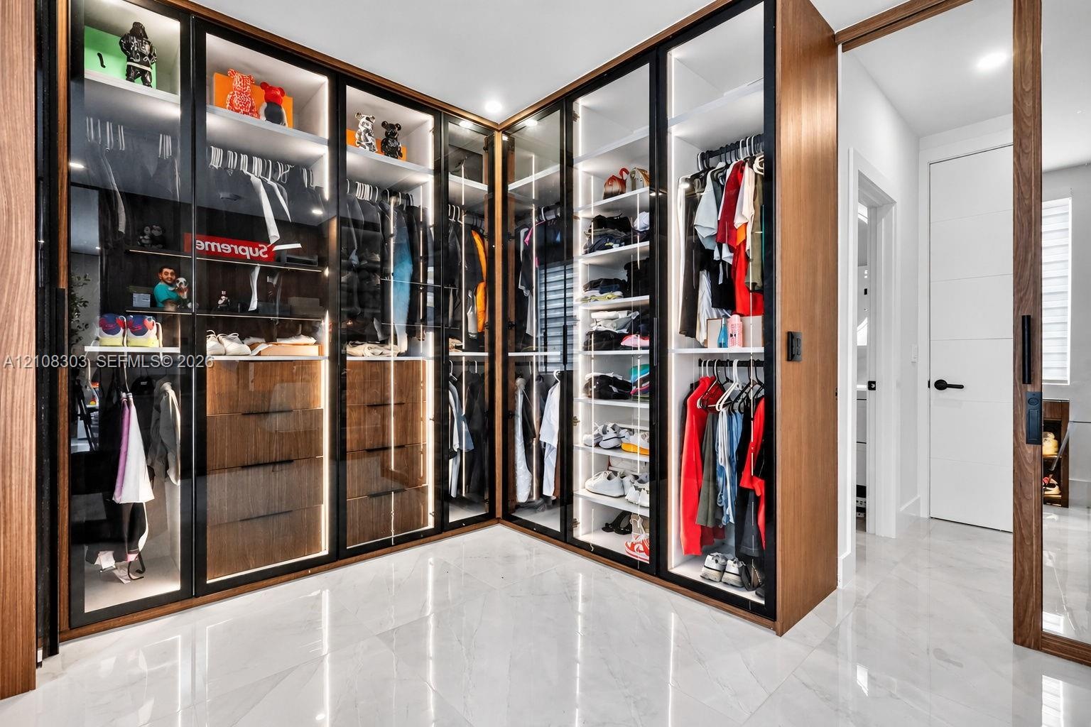 Custom built-in wardrobe featuring full-height glass-paneled doors, integrated LED accent lighting, wood-finish cabinetry, matte black hardware, and p