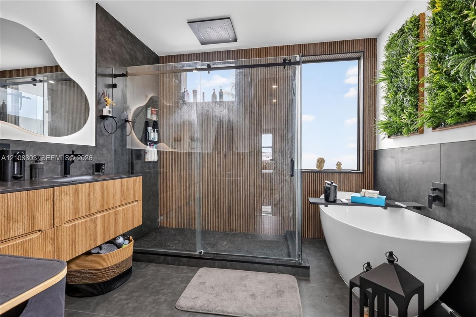 Bathroom featuring a floating wood-finish vanity with a dark countertop, a walk-in glass-enclosed shower with a rainfall showerhead, a freestanding so