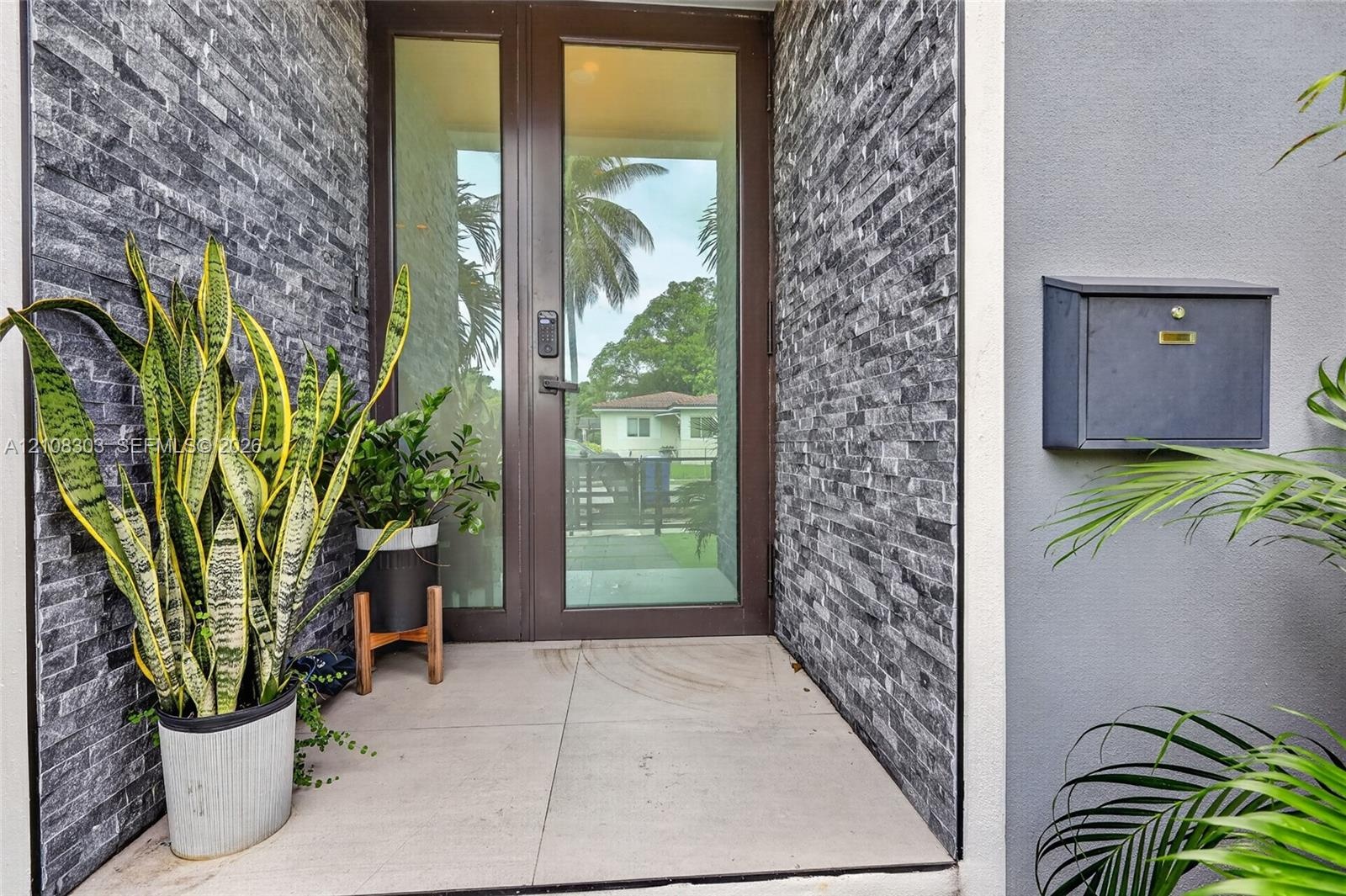 Entryway featuring a full-glass door with dark metal frame, charcoal-toned stacked stone accent walls, large-format tile flooring, and a wall-mounted 