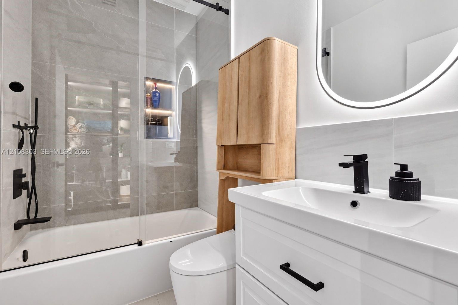 Bathroom featuring a glass-enclosed shower with large-format tile surround, recessed niche lighting, white vanity cabinet with matte black hardware, i