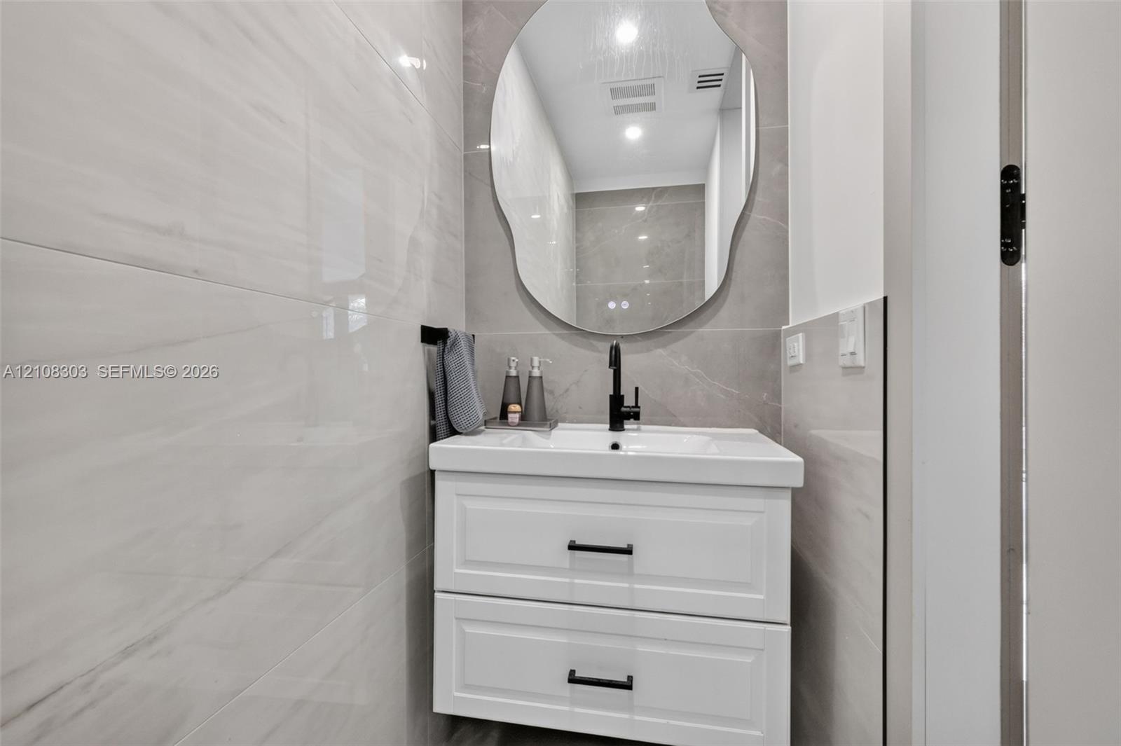 Wall-mounted white vanity with two drawers, rectangular basin, matte black faucet, and large organic-shaped mirror, featuring floor-to-ceiling large-f