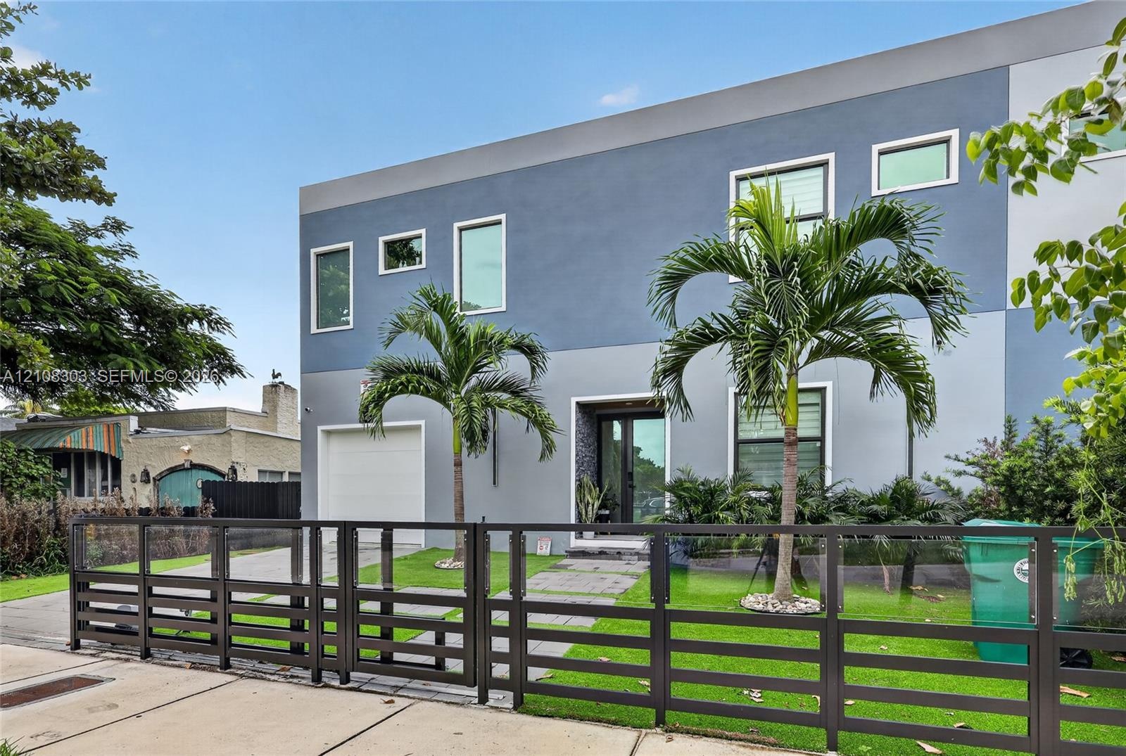 Modern two-story exterior featuring multi-tonal gray stucco finish, clean-lined horizontal metal fencing, a paved front walkway, and an attached singl