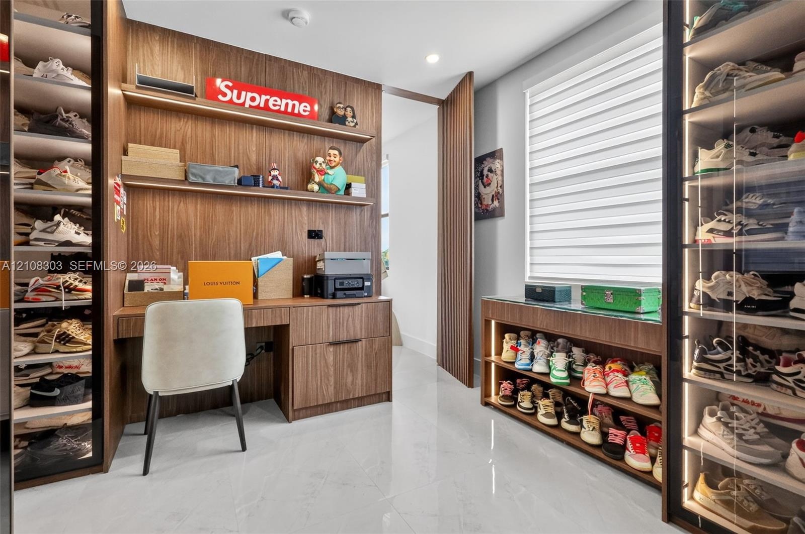 Custom wood-finish cabinetry featuring integrated shelving, built-in desk with drawer storage, glass-front display cases with internal lighting, and l