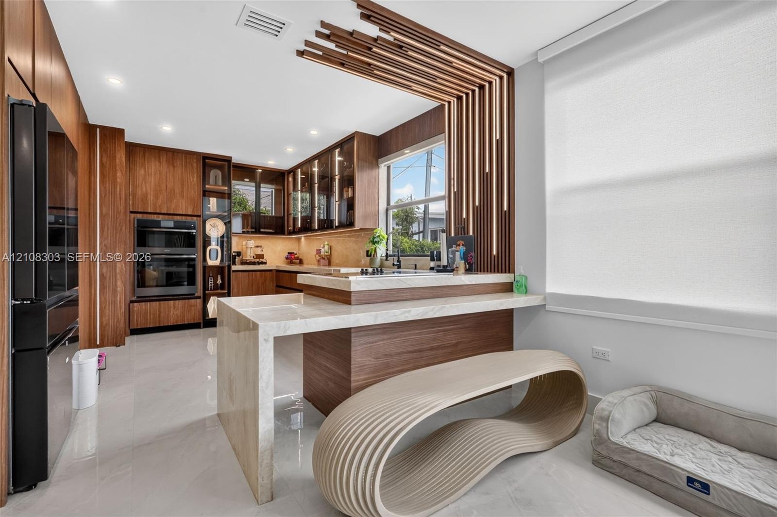 Kitchen featuring custom wood-veneer cabinetry, waterfall-edge stone countertop, integrated double wall ovens, and decorative slatted wood ceiling acc