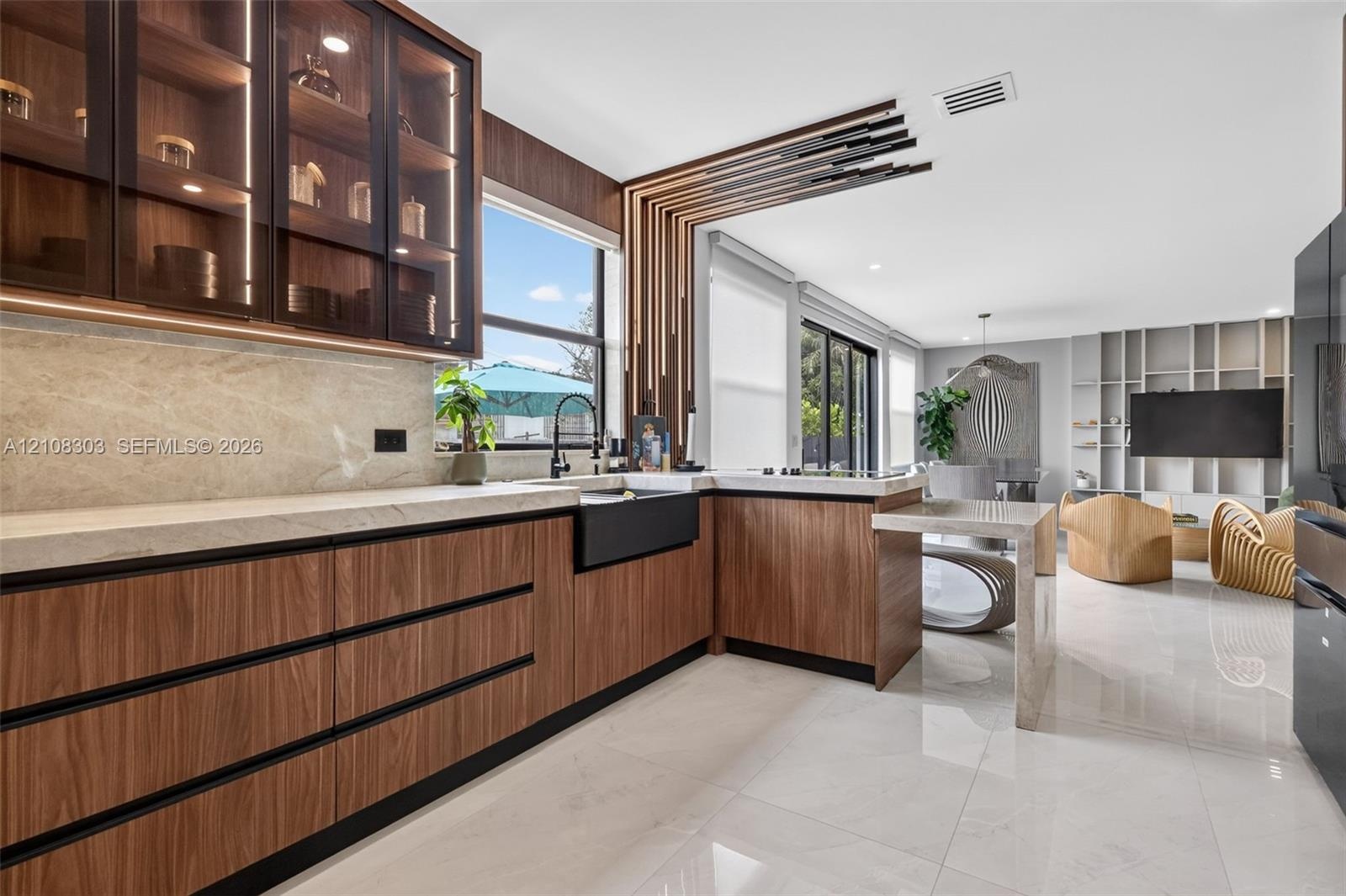 Modern kitchen featuring wood-finish cabinetry, stone countertops, a deep farmhouse-style sink, glass-front upper cabinetry with integrated lighting, 