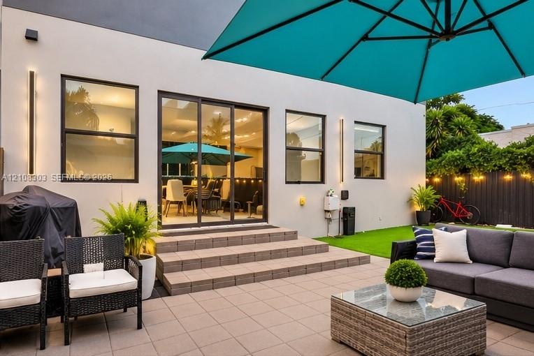 Patio area featuring light-toned tile flooring, three-step tiered entry, sliding glass doors, vertical exterior wall lighting, and an artificial grass