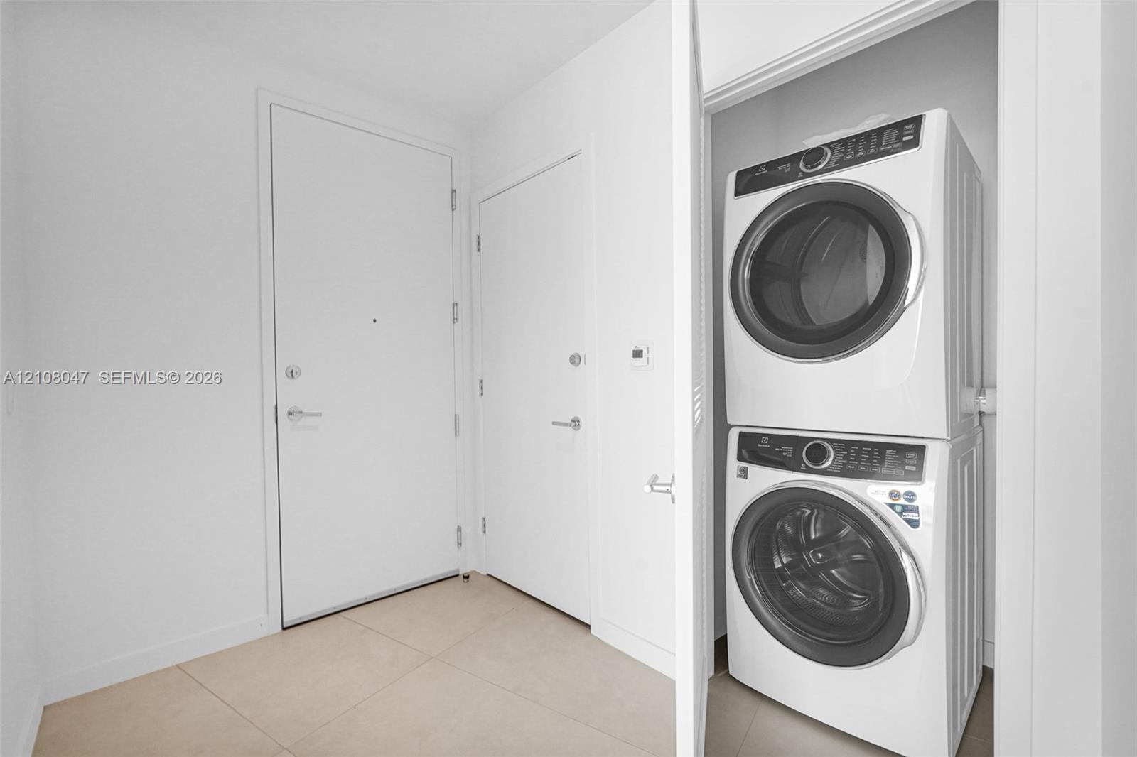 Stacked washer and dryer unit, smooth white walls, and light-toned floor tiling