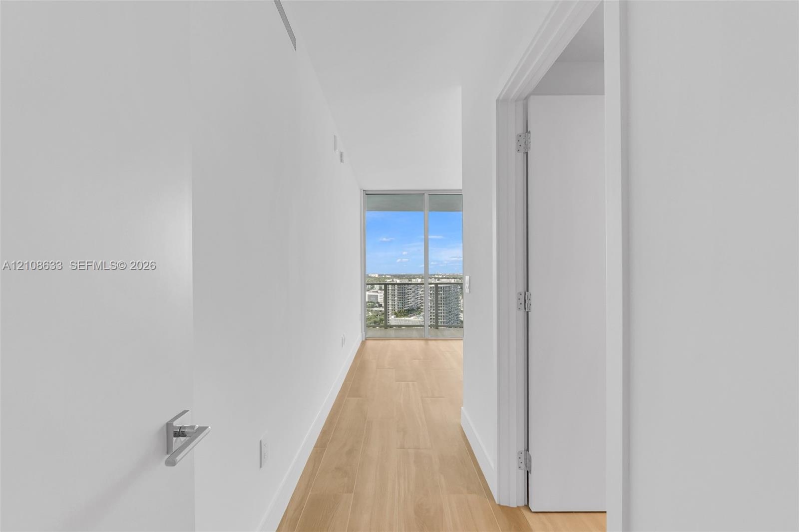 Hallway featuring wood-finish flooring, crisp white walls, and floor-to-ceiling glass paneling with an exterior railing