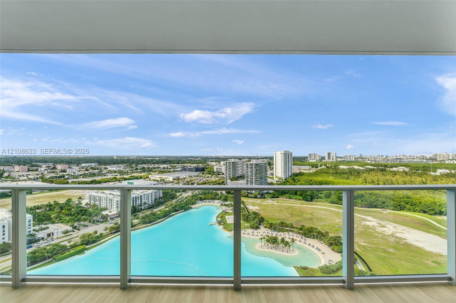Full-height glass balcony enclosure with metal framing, wood-finish flooring, and expansive panoramic scenery including a central lagoon