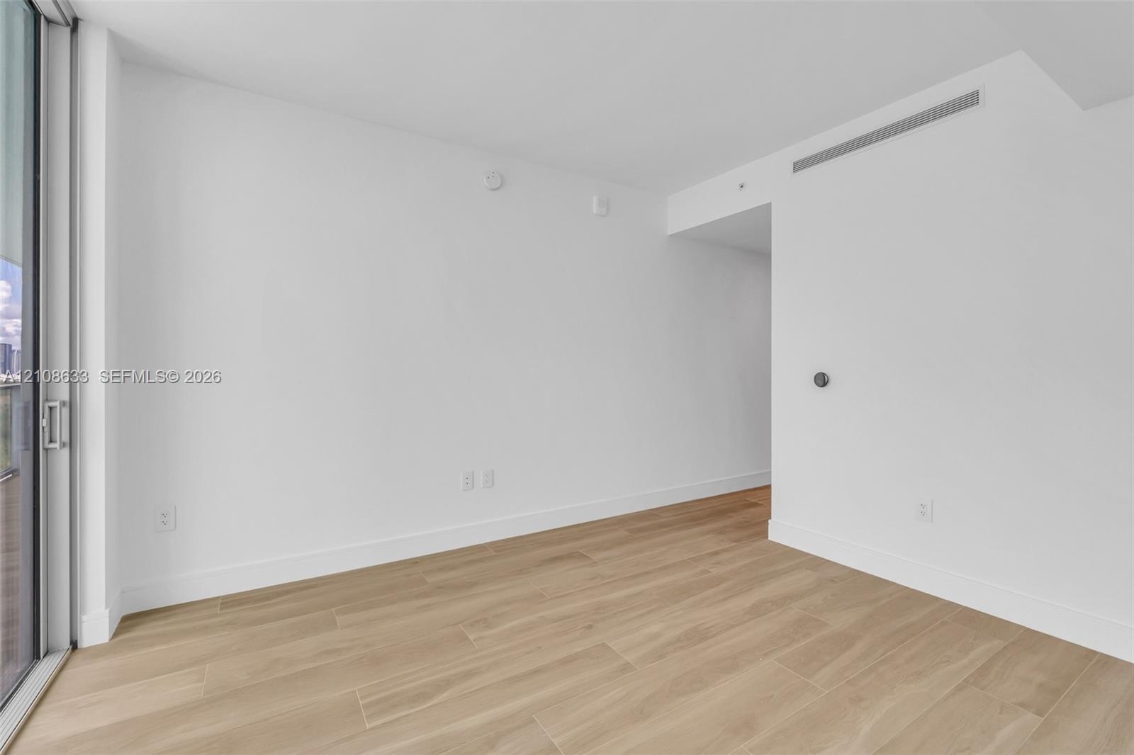 Neutral interior space featuring wood-finish tile flooring, floor-to-ceiling glass sliding door, and recessed ceiling HVAC system