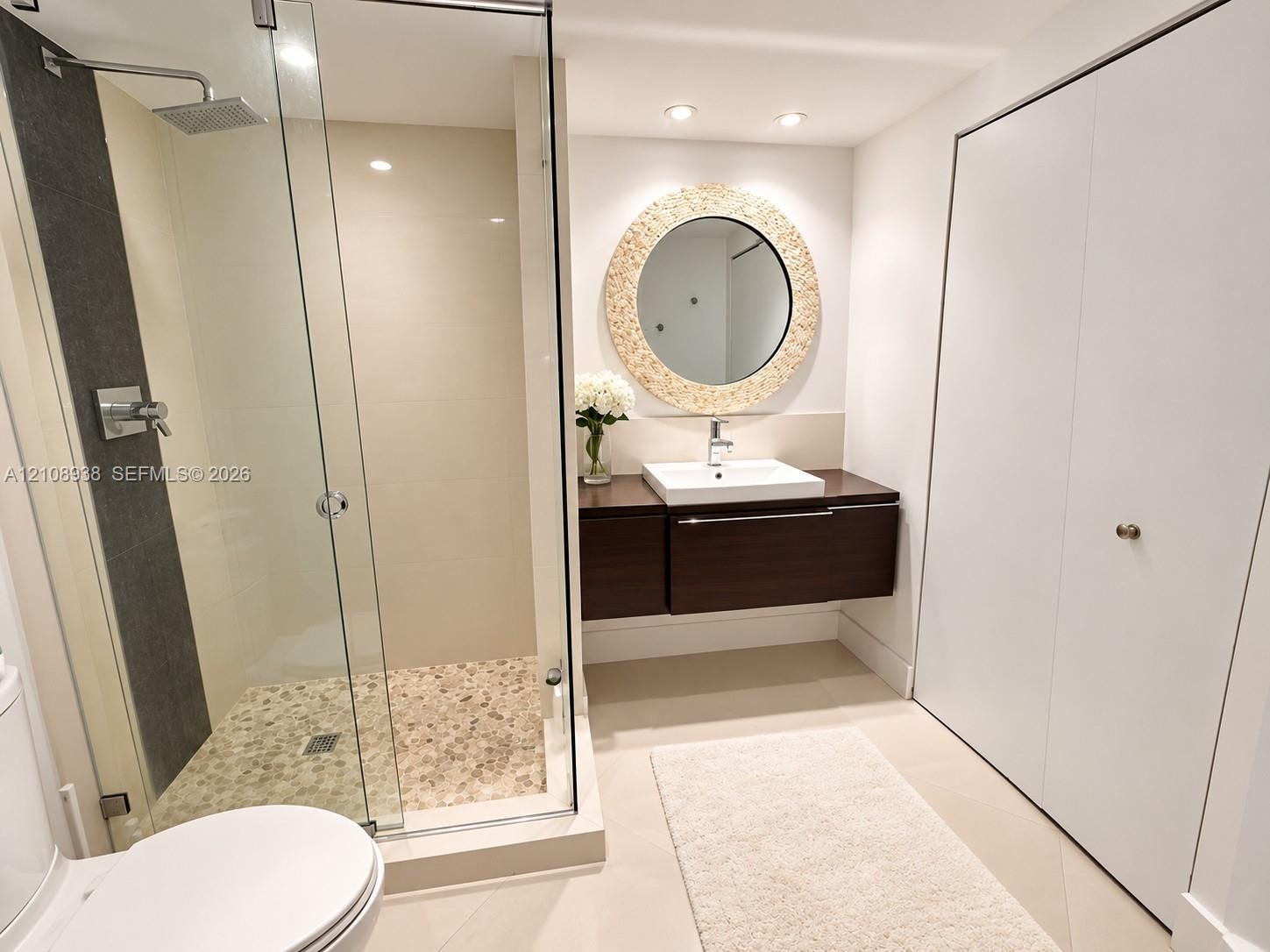 Floating dark wood-finish vanity with a rectangular vessel sink, glass-enclosed shower featuring a stone pebble floor, wall-mounted rainfall showerhea