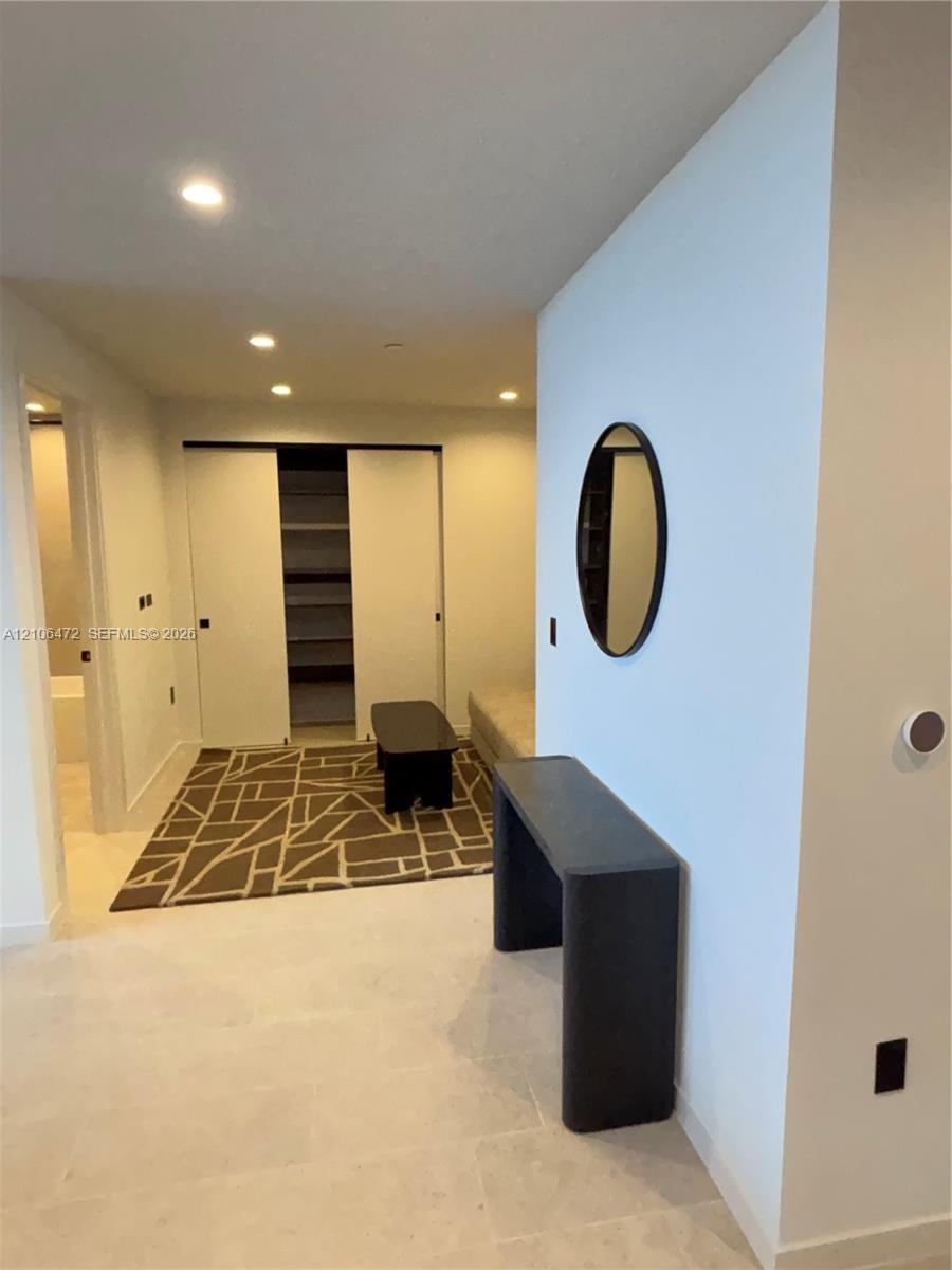 Built-in closet with sliding doors and integrated shelving, recessed lighting, and neutral stone-finish flooring