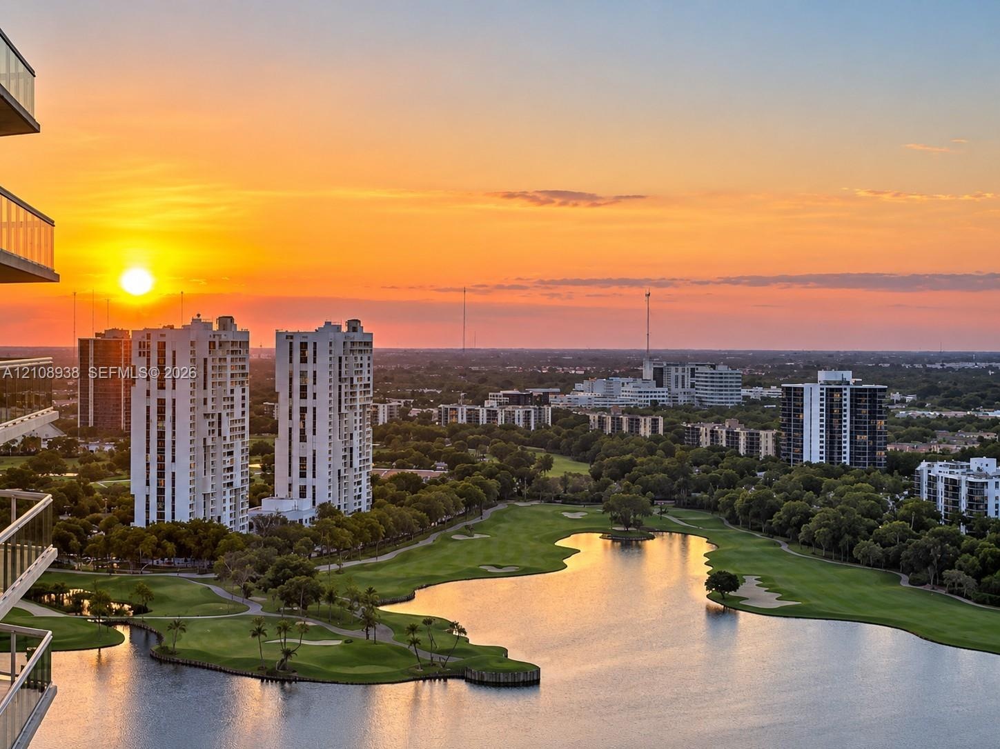 High-rise exterior featuring glass-railed balconies, overlooking a sprawling golf course, natural lake, and sunset horizon