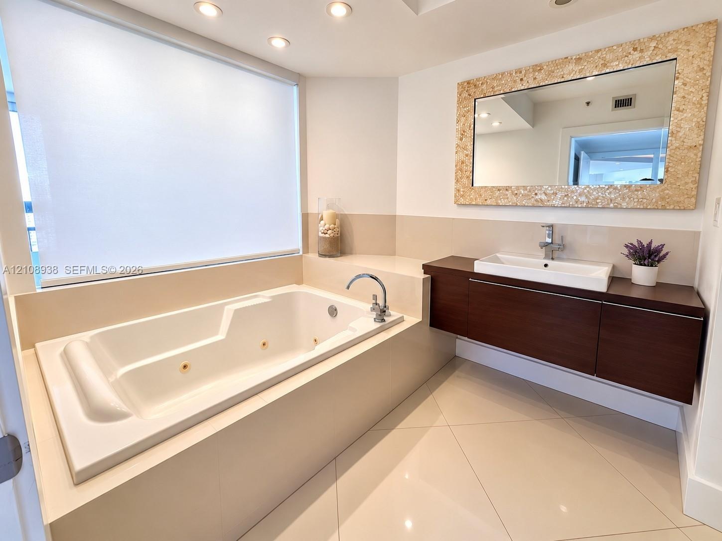 Bathroom featuring a jetted soaking tub, floating vanity with a rectangular vessel sink, large-format tile flooring, recessed ceiling lighting, and a 