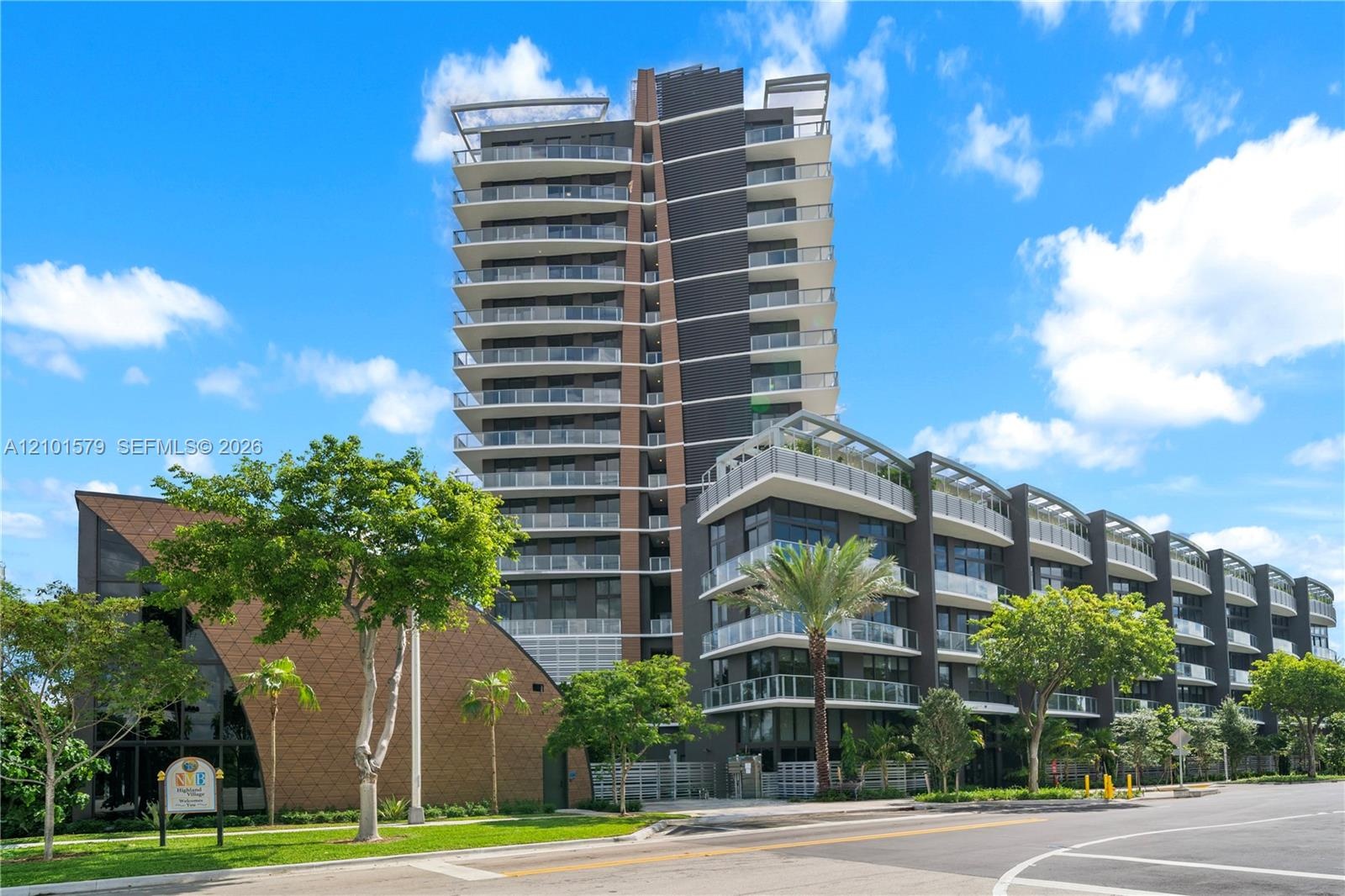Contemporary high-rise architecture featuring glass-railed private balconies, a multi-story facade with dark paneling, and an attached low-rise struct