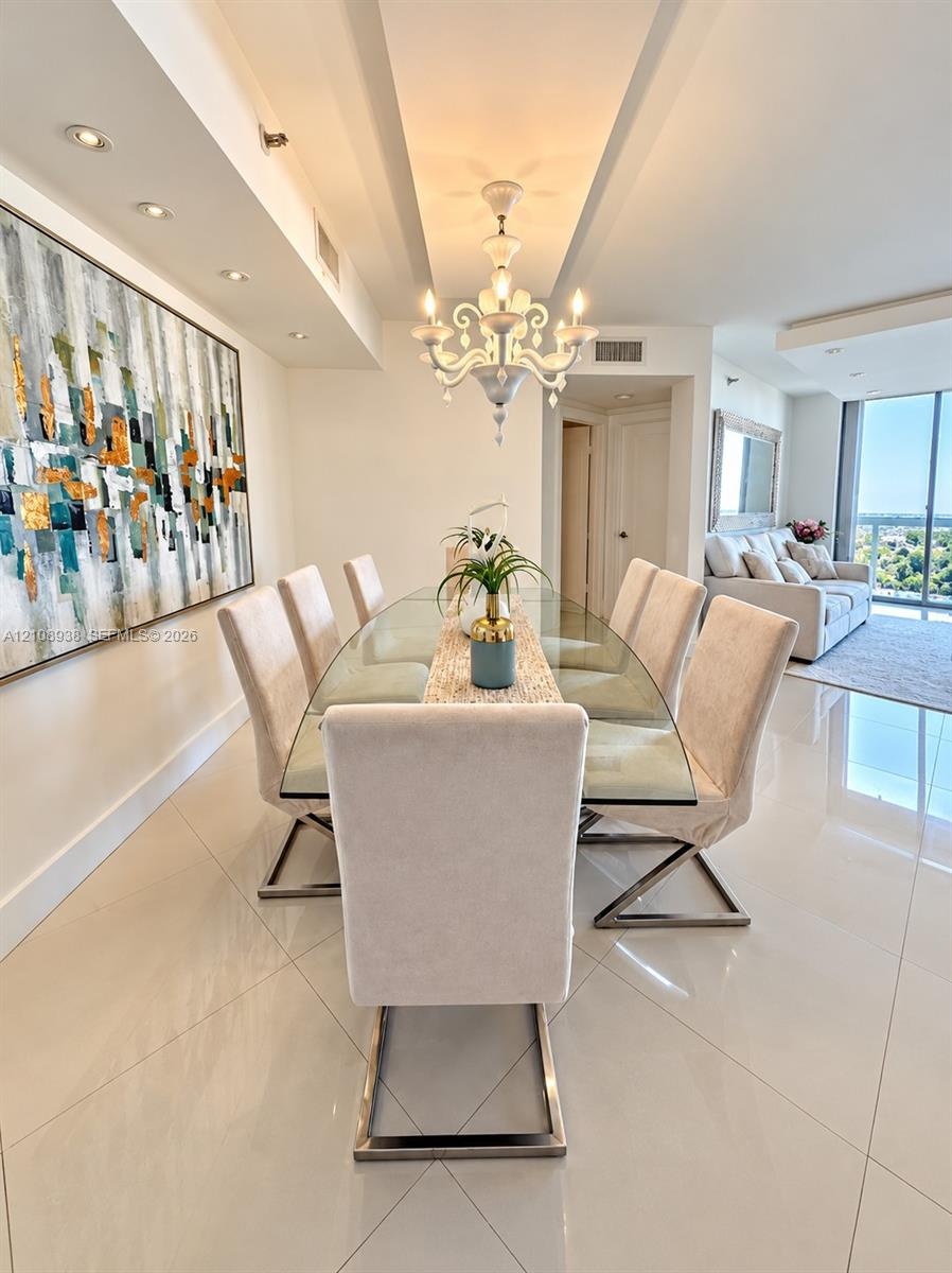 Dining area featuring polished large-format tile flooring, a decorative tiered chandelier, recessed accent lighting, and a recessed ceiling design