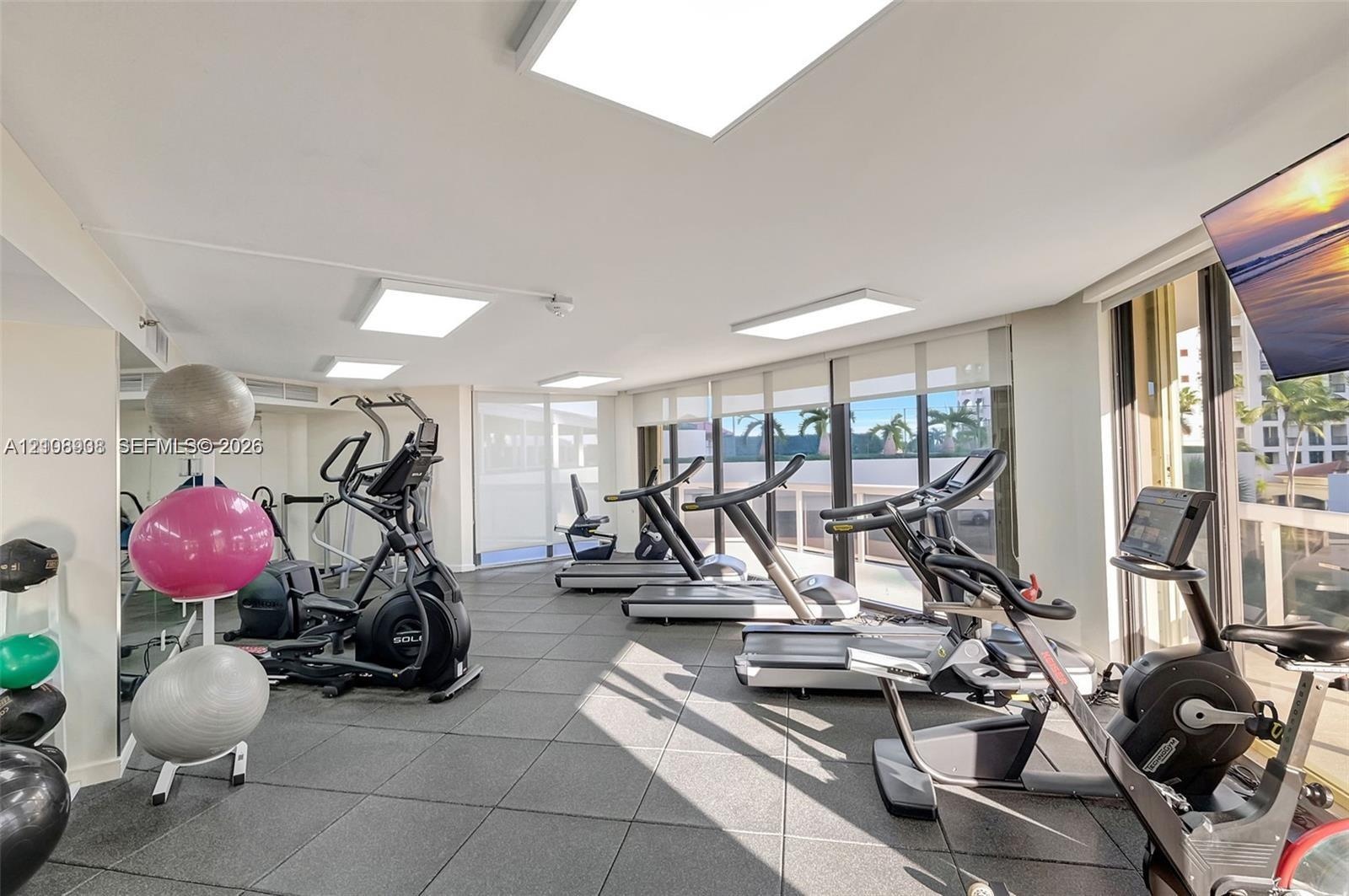 Fitness center featuring modular floor tiling, floor-to-ceiling windows, and recessed ceiling lighting