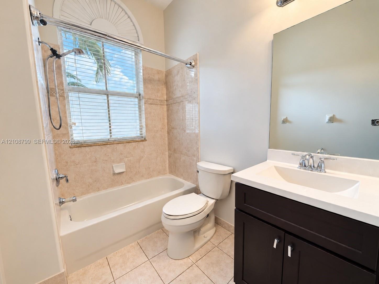 Bathroom featuring a dark wood-finish vanity with a white countertop and integrated sink, a tiled tub-shower combination, ceramic tile flooring, and a